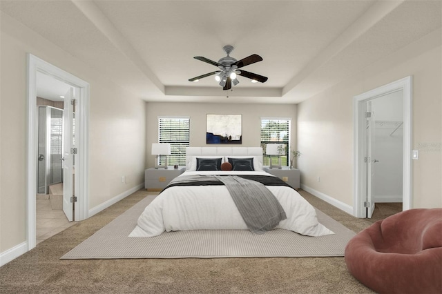 bedroom with carpet flooring, baseboards, a walk in closet, and a raised ceiling