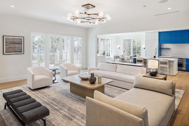 living room featuring french doors, light wood finished floors, baseboards, a notable chandelier, and wine cooler