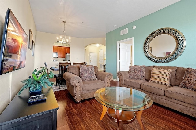 living area featuring arched walkways, dark wood-style flooring, a chandelier, and visible vents