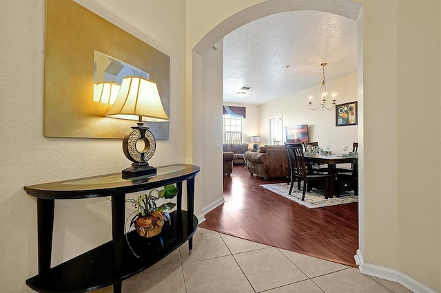 hall featuring a textured ceiling, arched walkways, baseboards, a chandelier, and tile patterned flooring