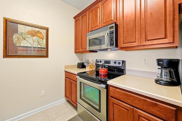 kitchen with light tile patterned floors, brown cabinetry, light countertops, and appliances with stainless steel finishes
