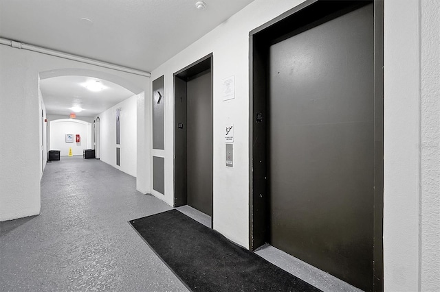 corridor featuring concrete flooring, arched walkways, and elevator