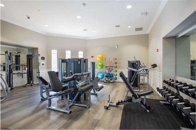 workout area featuring visible vents, a wainscoted wall, wood finished floors, and ornamental molding