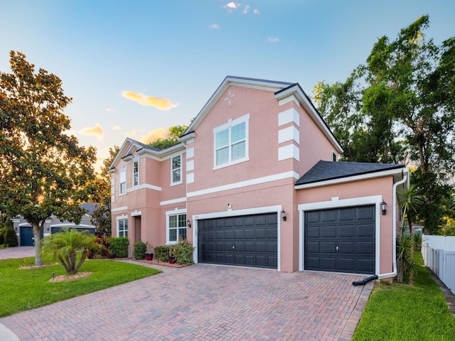 traditional-style house featuring fence, decorative driveway, a garage, stucco siding, and a front lawn
