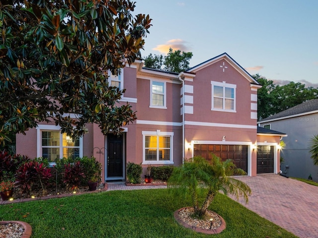 traditional-style home with a front lawn, stucco siding, decorative driveway, and an attached garage