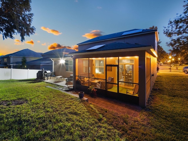 rear view of house with a patio, a sunroom, fence, solar panels, and a yard