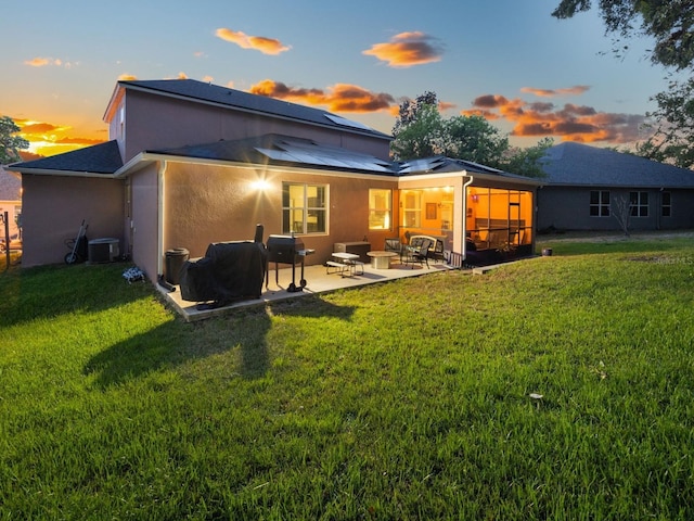 back of house at dusk with stucco siding, solar panels, a lawn, and a patio