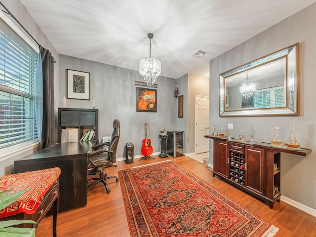 office with baseboards, a chandelier, visible vents, and wood finished floors