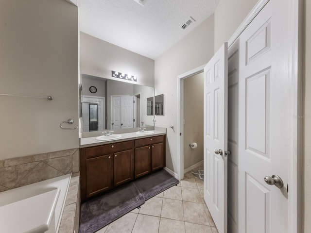 full bathroom featuring double vanity, tile patterned flooring, tiled tub, and a sink