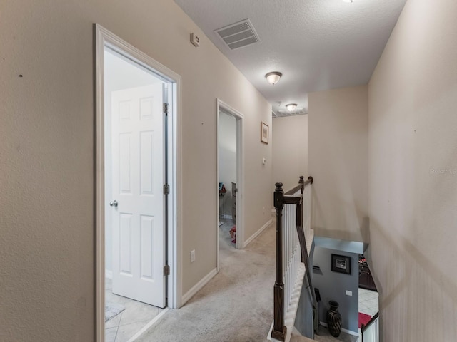 hall featuring a textured ceiling, an upstairs landing, visible vents, light carpet, and baseboards