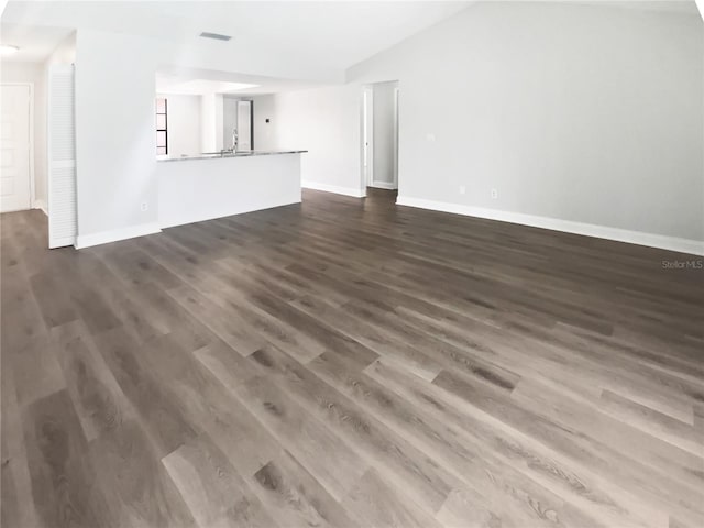 unfurnished living room with a sink, dark wood-style flooring, vaulted ceiling, visible vents, and baseboards
