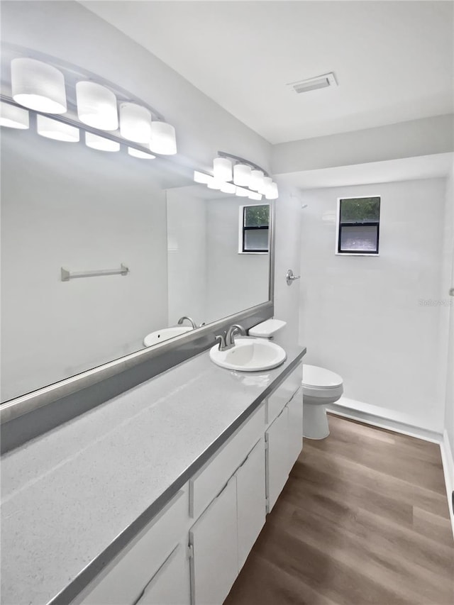 bathroom featuring vanity, visible vents, toilet, wood finished floors, and baseboards