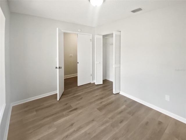 unfurnished bedroom featuring visible vents, wood finished floors, baseboards, and a closet