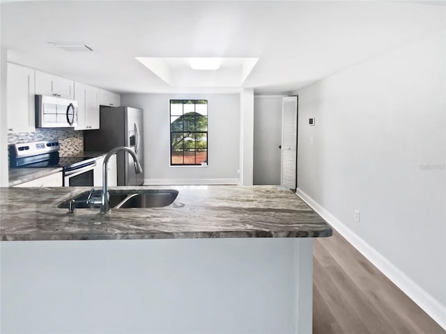 kitchen with white cabinets, a sink, decorative backsplash, a peninsula, and appliances with stainless steel finishes