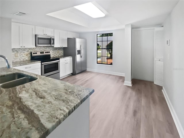 kitchen featuring a sink, light wood-style floors, stainless steel appliances, backsplash, and light stone countertops