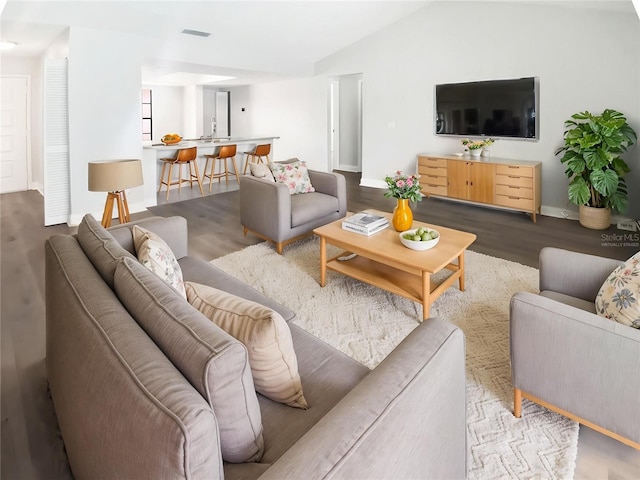 living area with visible vents, baseboards, vaulted ceiling, and wood finished floors