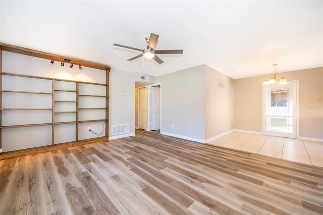 empty room with visible vents, light wood-type flooring, baseboards, and ceiling fan with notable chandelier