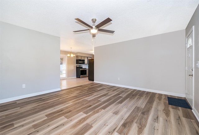 unfurnished living room with light wood-style flooring, baseboards, and ceiling fan with notable chandelier