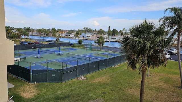 view of tennis court with a water view, fence, and a yard