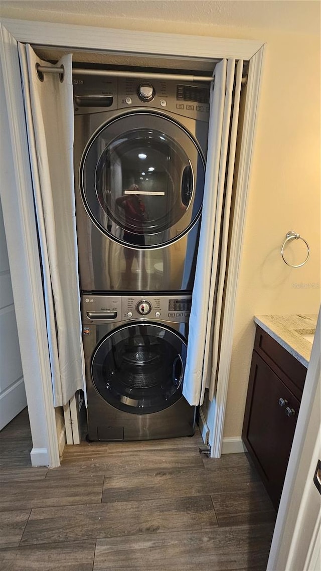 laundry room with baseboards, dark wood-style flooring, stacked washer and dryer, and laundry area