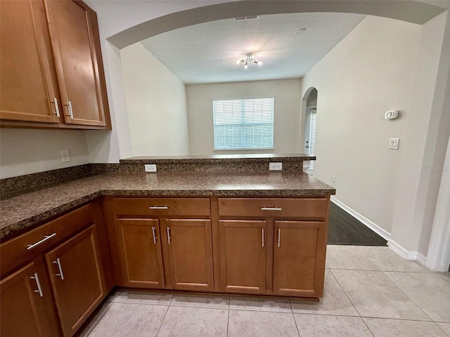 8271 Maritime Flag St Unit 125, Windermere, FL 34786 - kitchen featuring arched walkways, dark countertops, a peninsula, brown cabinets, and light tile patterned flooring