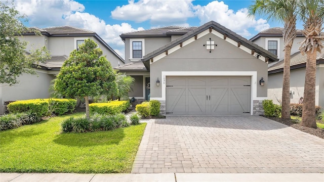view of front of property featuring a front lawn, stone siding, a garage, stucco siding, and decorative driveway