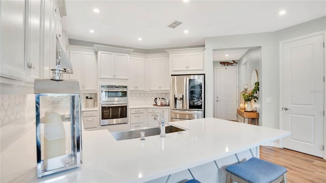 kitchen with a kitchen breakfast bar, backsplash, appliances with stainless steel finishes, a sink, and white cabinets