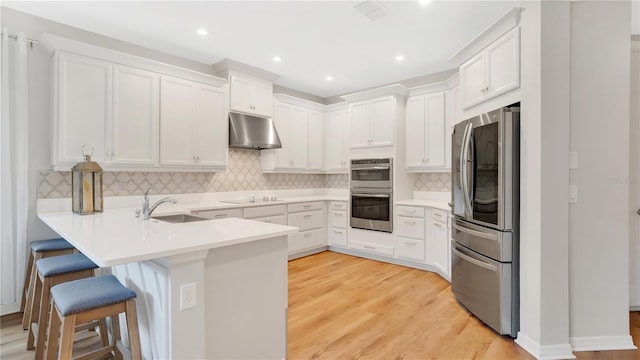 kitchen featuring a peninsula, a breakfast bar, under cabinet range hood, a sink, and appliances with stainless steel finishes