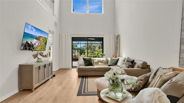 living area featuring baseboards, visible vents, light wood-style flooring, and a towering ceiling