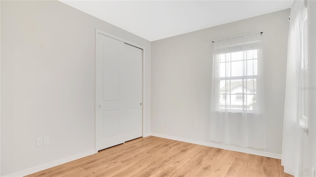 unfurnished bedroom featuring baseboards, a closet, and light wood-type flooring