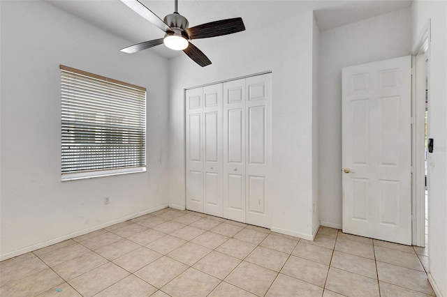unfurnished bedroom with light tile patterned floors, ceiling fan, a closet, and baseboards