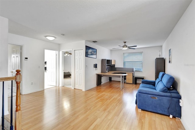 living area with visible vents, light wood-type flooring, a ceiling fan, and baseboards