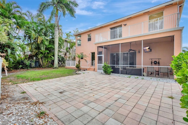 back of property with a sunroom, a yard, a patio, a balcony, and stucco siding