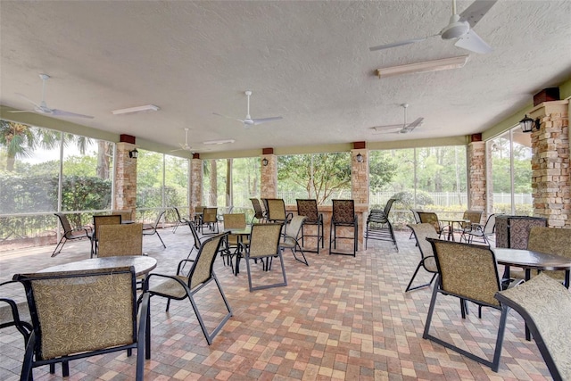 exterior space featuring outdoor dining space, a ceiling fan, brick patterned floor, and a textured ceiling