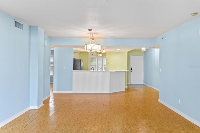 2700 N Peninsula Ave Unit 215, New Smyrna Beach, FL 32169 - unfurnished living room featuring light wood finished floors, baseboards, visible vents, and an inviting chandelier