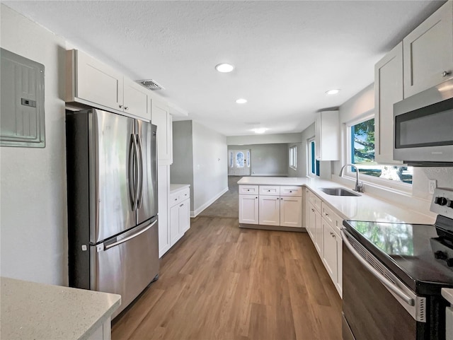 kitchen with a sink, stainless steel appliances, light wood-style flooring, a peninsula, and visible vents