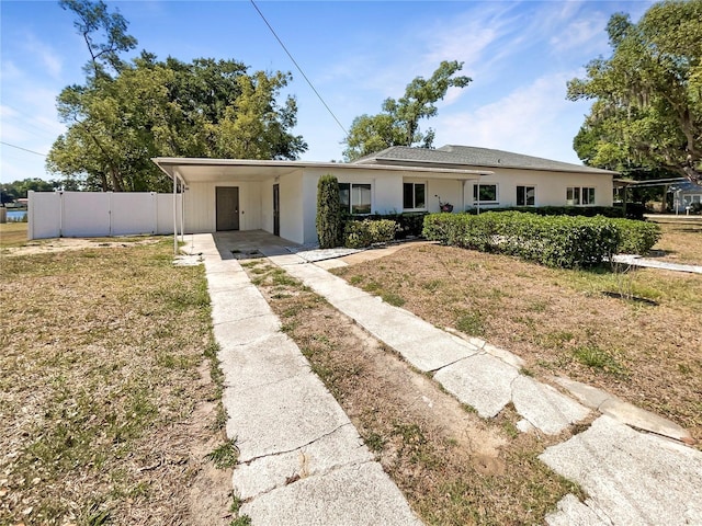 view of front of property with an attached carport, driveway, fence, a front yard, and stucco siding