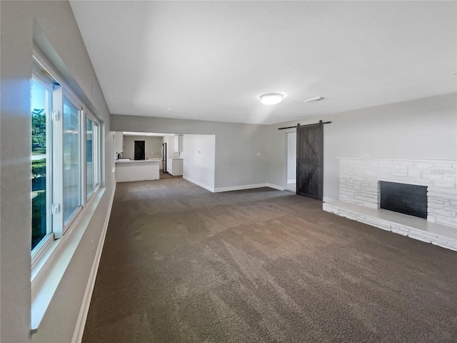 unfurnished living room featuring a barn door, a stone fireplace, baseboards, and carpet floors