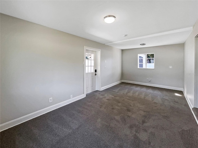 unfurnished room with baseboards, dark colored carpet, and plenty of natural light
