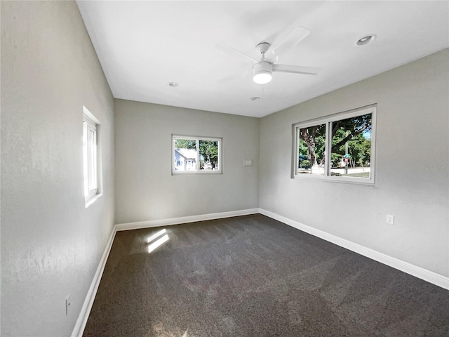spare room with baseboards, dark carpet, and a ceiling fan