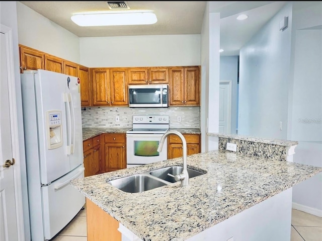 kitchen with a sink, brown cabinets, decorative backsplash, light tile patterned flooring, and white appliances