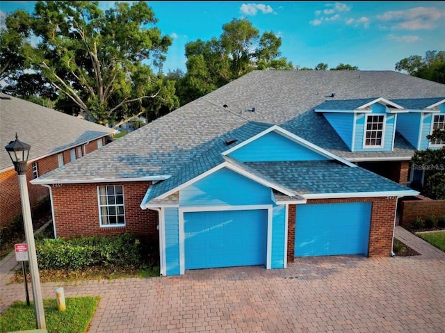 view of front facade featuring brick siding, driveway, an attached garage, and roof with shingles