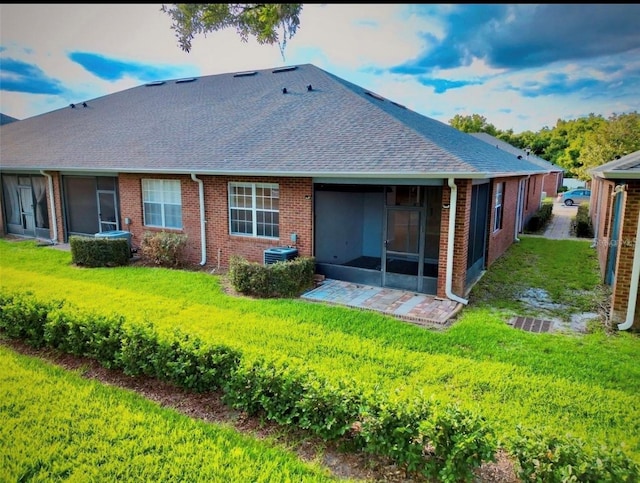 back of house featuring a sunroom, a lawn, a shingled roof, and brick siding