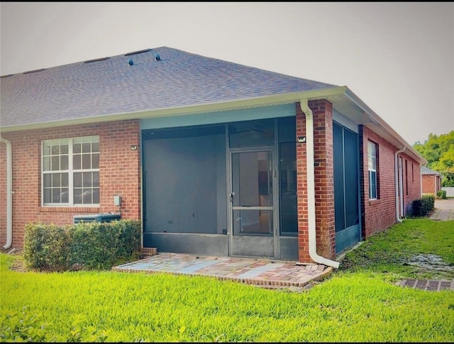 back of property featuring a lawn, a shingled roof, a sunroom, and brick siding