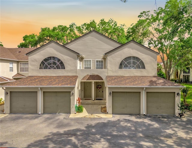 view of front of property with stucco siding, an attached garage, driveway, and a shingled roof