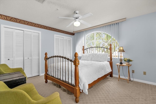 carpeted bedroom with two closets, baseboards, and a ceiling fan