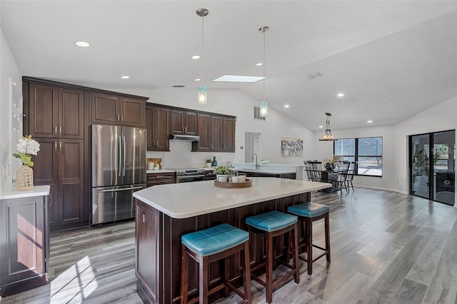 kitchen featuring stainless steel appliances, light wood-style flooring, dark brown cabinets, light countertops, and a kitchen island