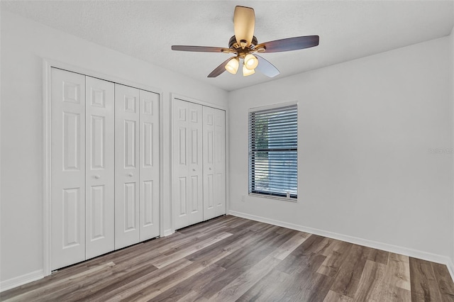 unfurnished bedroom with baseboards, wood finished floors, and multiple closets