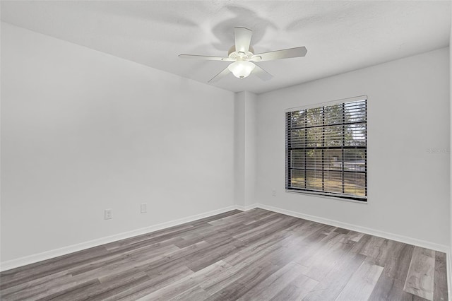 unfurnished room with wood finished floors, a ceiling fan, and baseboards