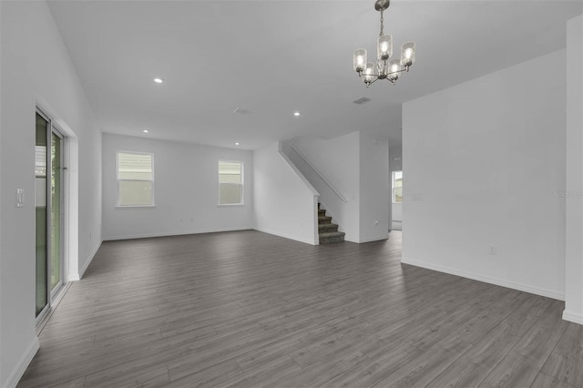 unfurnished living room featuring recessed lighting, dark wood-type flooring, baseboards, stairs, and a notable chandelier